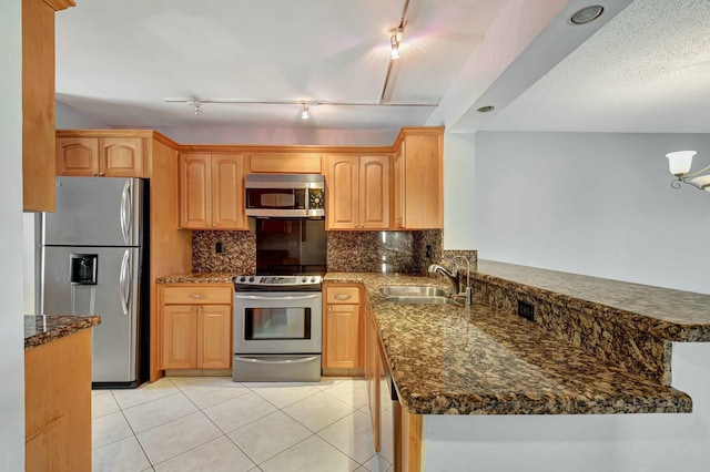 kitchen featuring dark stone countertops, appliances with stainless steel finishes, kitchen peninsula, light tile patterned floors, and sink