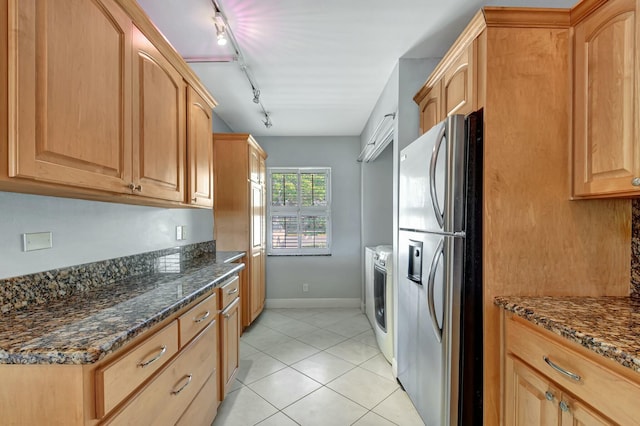 kitchen with dark stone countertops, stainless steel fridge with ice dispenser, washer / dryer, light brown cabinetry, and light tile patterned flooring