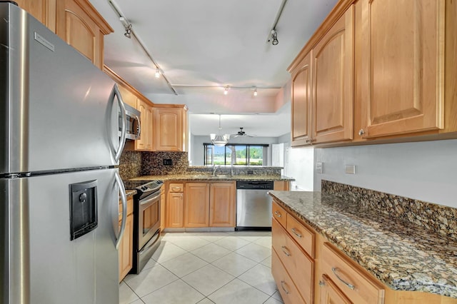 kitchen with dark stone countertops, rail lighting, appliances with stainless steel finishes, light tile patterned floors, and ceiling fan