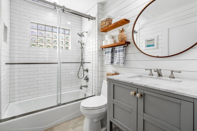 full bathroom with toilet, vanity, wooden walls, and shower / bath combination with glass door