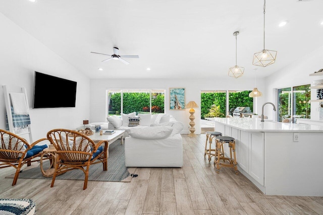 living room with ceiling fan, plenty of natural light, vaulted ceiling, and light hardwood / wood-style flooring