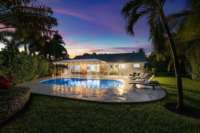 pool at dusk featuring a yard and a patio