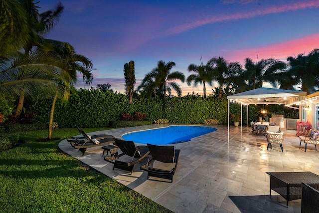 pool at dusk with exterior kitchen and a patio area