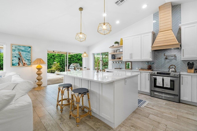 kitchen featuring premium range hood, white cabinetry, tasteful backsplash, electric range, and a kitchen island with sink