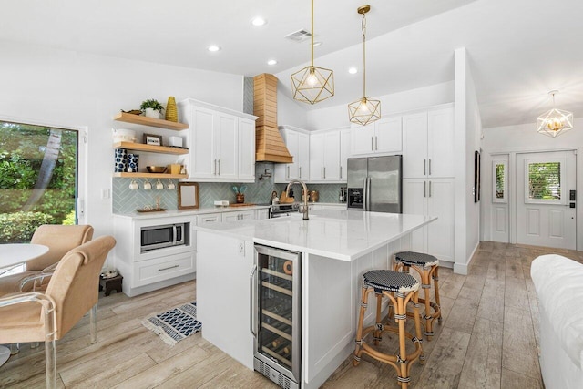 kitchen featuring wine cooler, lofted ceiling, white cabinetry, an island with sink, and stainless steel appliances