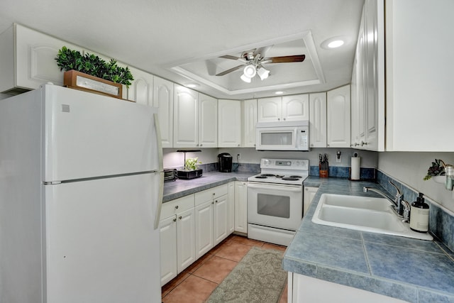 kitchen with white appliances, white cabinetry, sink, light tile patterned floors, and a tray ceiling