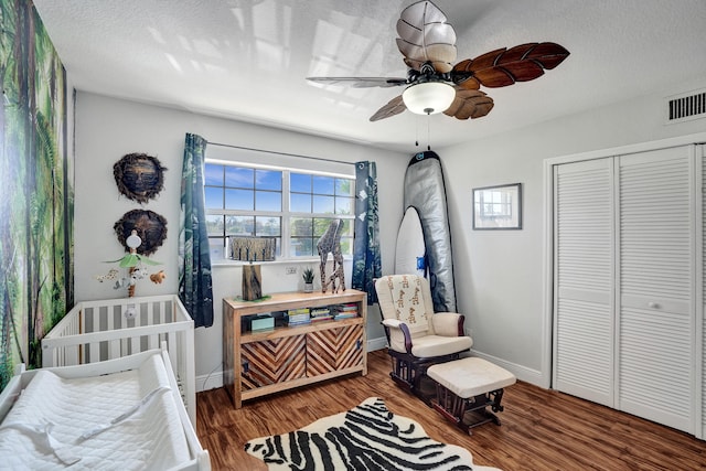 bedroom featuring a textured ceiling, wood-type flooring, a closet, ceiling fan, and a nursery area