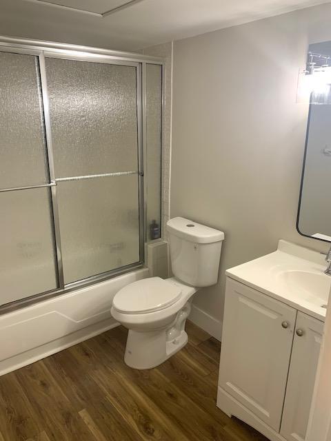 full bathroom featuring toilet, enclosed tub / shower combo, wood-type flooring, and vanity