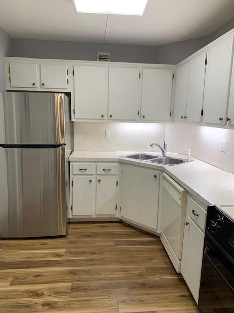 kitchen with white cabinets, stainless steel refrigerator, white dishwasher, black range oven, and sink