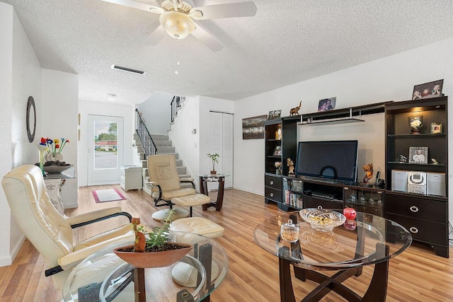 living room featuring light wood-type flooring, ceiling fan, and a textured ceiling