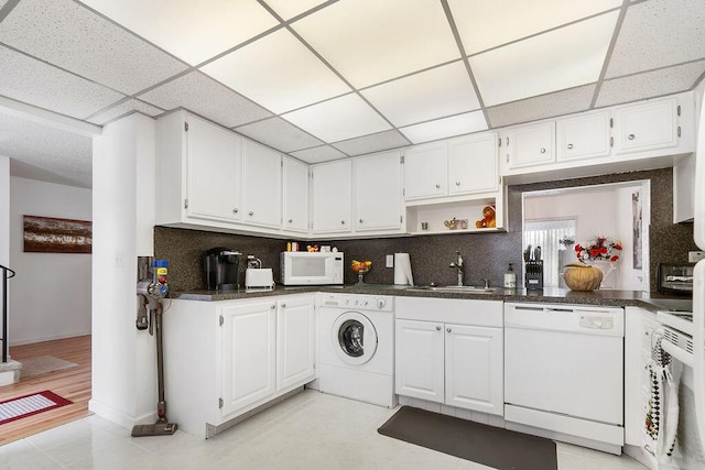 kitchen with white appliances, washer / dryer, decorative backsplash, white cabinets, and sink