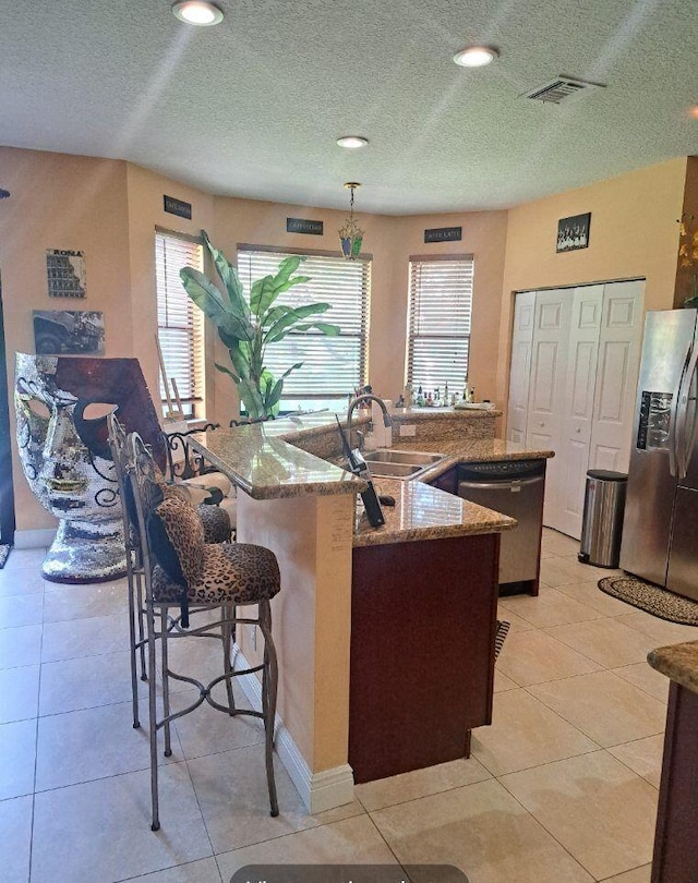 kitchen with a center island with sink, sink, hanging light fixtures, stainless steel appliances, and light tile patterned floors