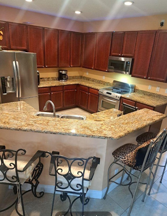 kitchen featuring appliances with stainless steel finishes, sink, light stone counters, a breakfast bar, and light tile patterned floors