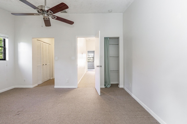 unfurnished bedroom featuring ceiling fan, light carpet, a textured ceiling, and a high ceiling