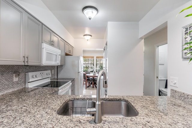 kitchen with white appliances, light stone counters, decorative backsplash, gray cabinetry, and sink