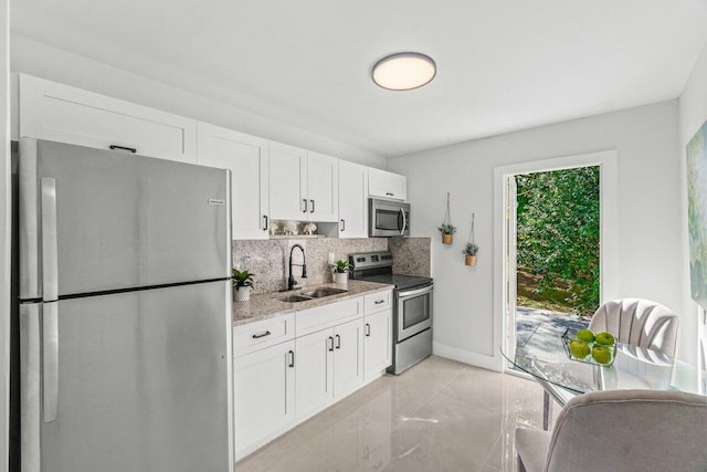 kitchen with white cabinets, appliances with stainless steel finishes, decorative backsplash, sink, and light stone counters