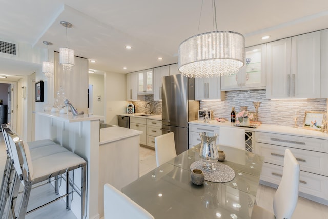 kitchen featuring a chandelier, hanging light fixtures, tasteful backsplash, white cabinets, and appliances with stainless steel finishes