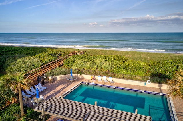 view of swimming pool with a water view, a view of the beach, and a patio