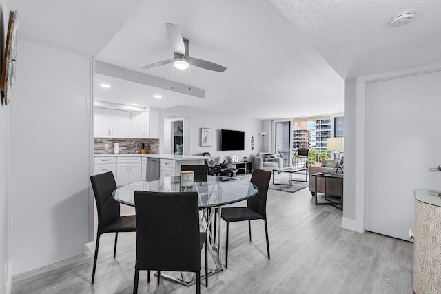 dining area with ceiling fan, a textured ceiling, a wall of windows, and light hardwood / wood-style flooring