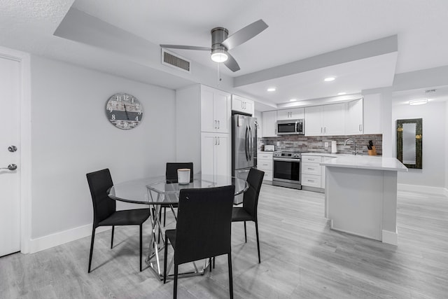 dining space with ceiling fan, light hardwood / wood-style floors, a raised ceiling, and sink