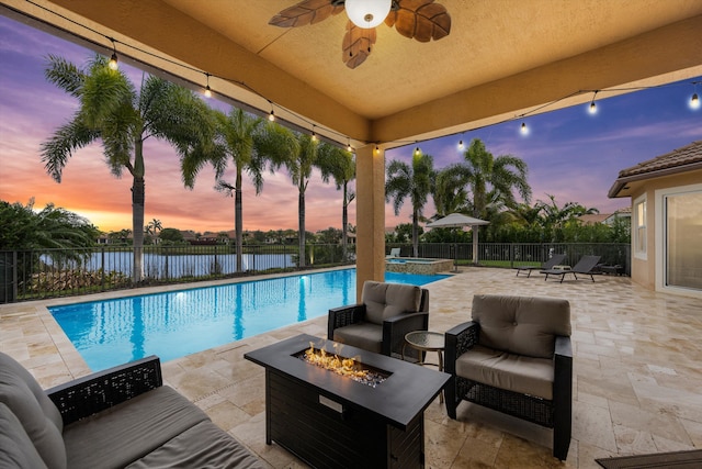 pool at dusk featuring an outdoor living space with a fire pit, a patio, and a water view