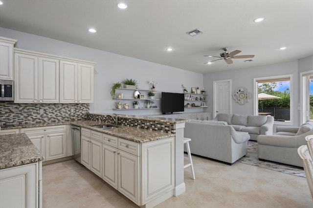 kitchen with sink, dark stone countertops, decorative backsplash, kitchen peninsula, and stainless steel appliances