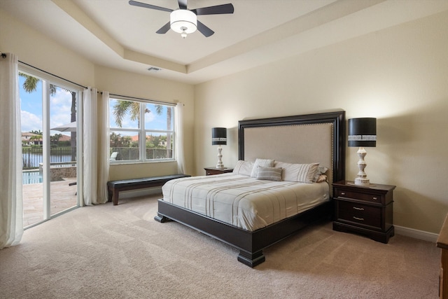 carpeted bedroom featuring a water view, ceiling fan, access to exterior, and a raised ceiling