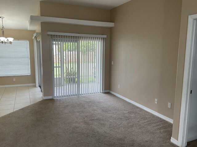 carpeted empty room with tile patterned floors, a notable chandelier, and baseboards