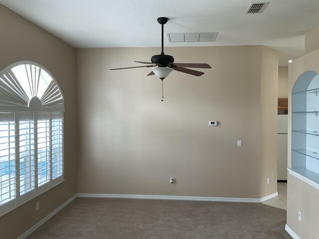 empty room with visible vents, light colored carpet, a ceiling fan, and baseboards