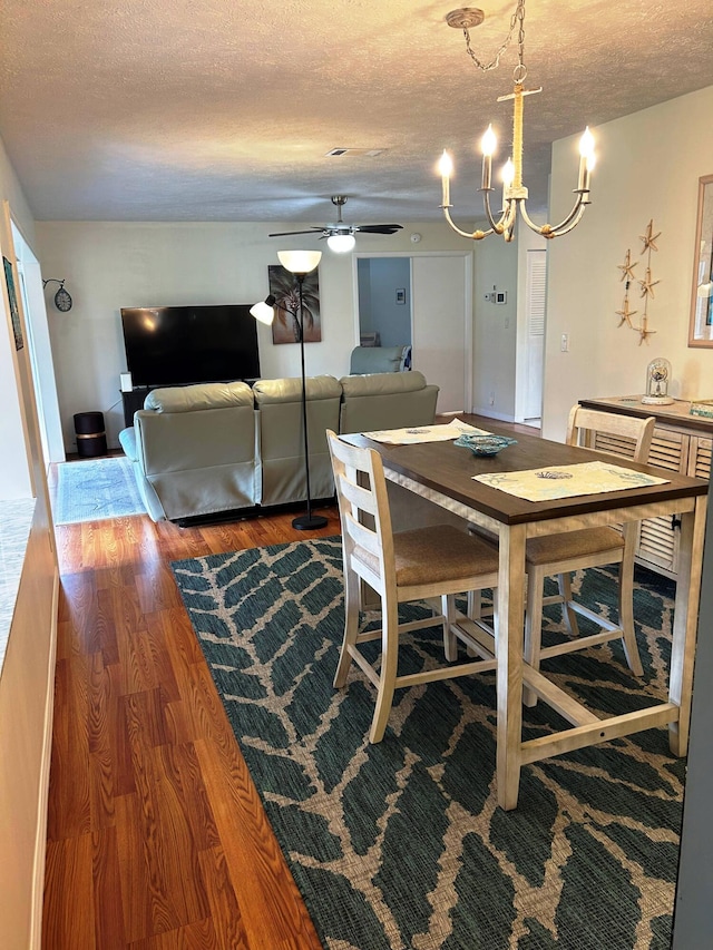 dining room with wood-type flooring, ceiling fan with notable chandelier, and a textured ceiling