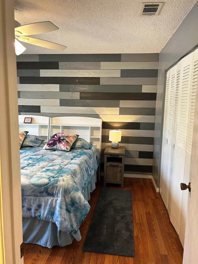 bedroom with wooden walls, dark hardwood / wood-style floors, a closet, and a textured ceiling