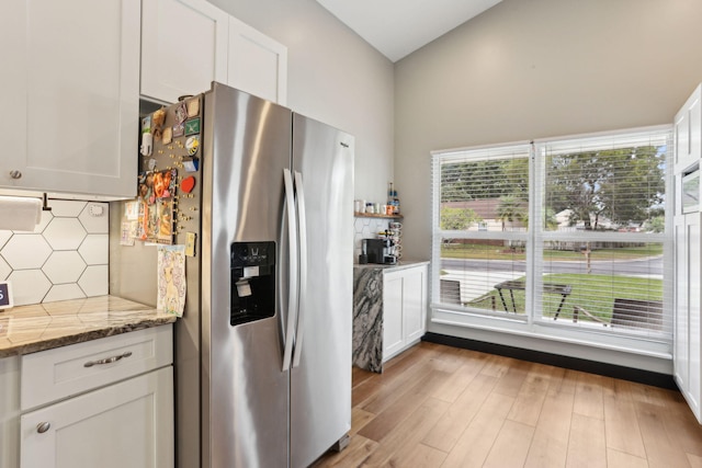 kitchen with stainless steel refrigerator with ice dispenser, backsplash, white cabinetry, and stone counters