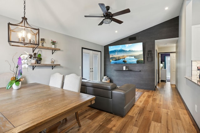 living room with ceiling fan with notable chandelier, light hardwood / wood-style flooring, and vaulted ceiling