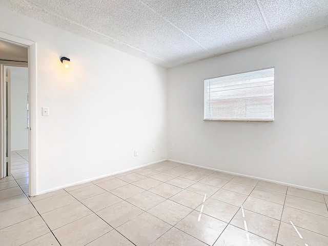 spare room featuring light tile patterned floors, baseboards, and a textured ceiling