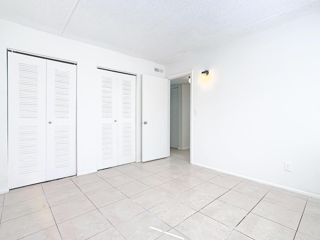 unfurnished bedroom featuring light tile patterned floors, visible vents, two closets, and a textured ceiling