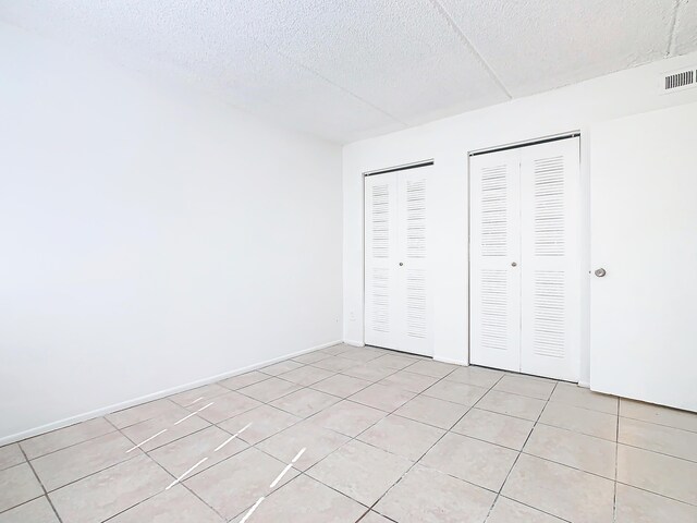 unfurnished bedroom featuring visible vents, multiple closets, a textured ceiling, light tile patterned floors, and baseboards