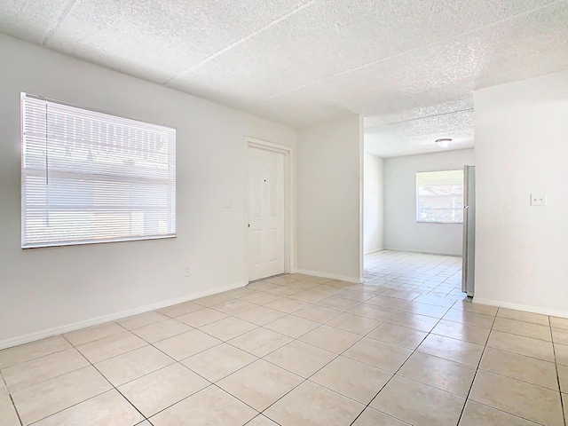 spare room featuring light tile patterned floors, baseboards, and a textured ceiling