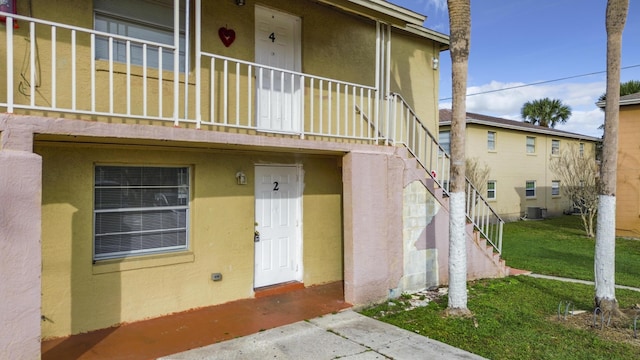 property entrance featuring stucco siding, cooling unit, and a yard