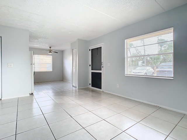 spare room with light tile patterned floors, baseboards, a textured ceiling, and a ceiling fan