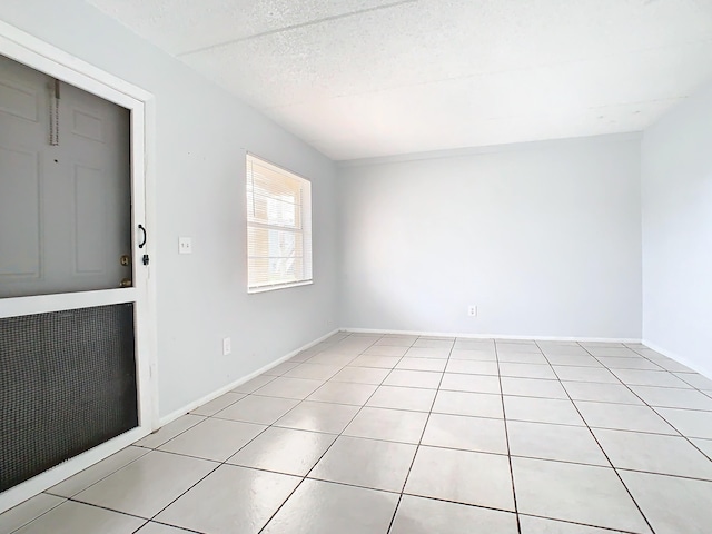 spare room with baseboards, a textured ceiling, and light tile patterned flooring