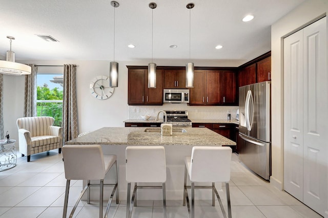 kitchen featuring sink, light stone counters, a center island with sink, pendant lighting, and appliances with stainless steel finishes