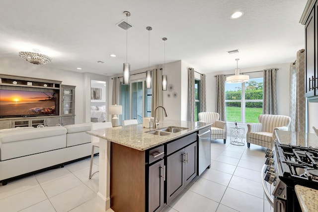 kitchen featuring light stone countertops, pendant lighting, an island with sink, appliances with stainless steel finishes, and sink