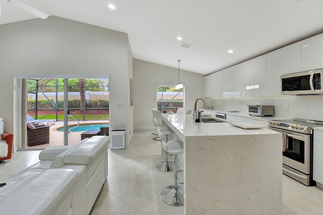 kitchen with pendant lighting, lofted ceiling, a kitchen island with sink, appliances with stainless steel finishes, and sink