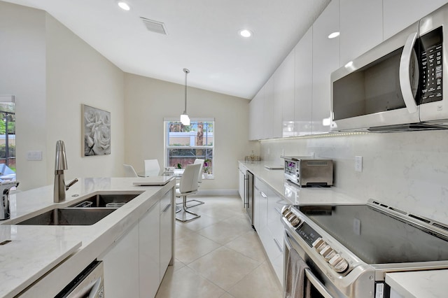 kitchen with vaulted ceiling, pendant lighting, white cabinets, appliances with stainless steel finishes, and sink