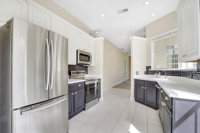 kitchen featuring stainless steel appliances, light tile patterned floors, decorative backsplash, white cabinets, and sink