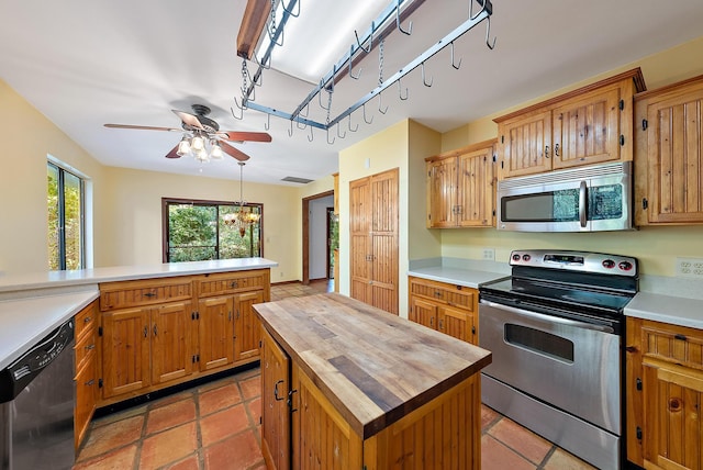 kitchen with kitchen peninsula, a kitchen island, pendant lighting, stainless steel appliances, and ceiling fan with notable chandelier