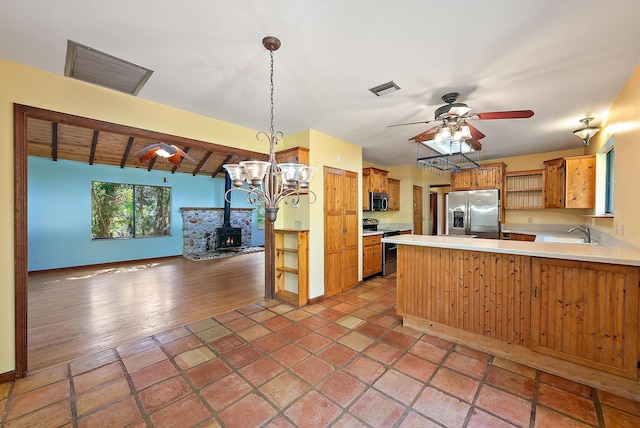 kitchen featuring stainless steel appliances, decorative light fixtures, kitchen peninsula, beamed ceiling, and a wood stove