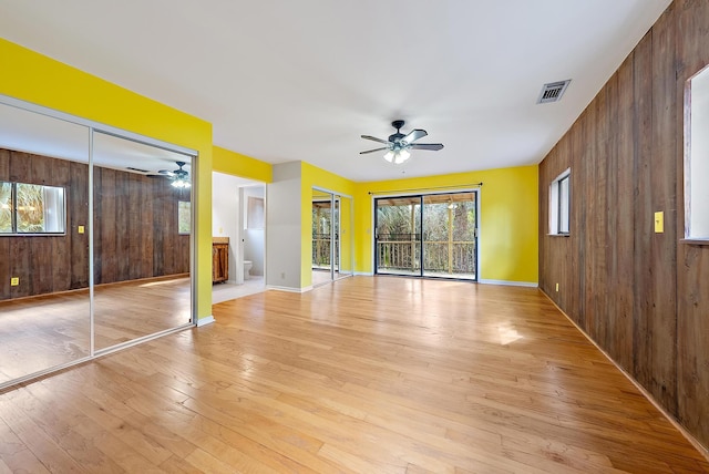 unfurnished bedroom featuring ceiling fan, ensuite bathroom, light wood-type flooring, and wood walls