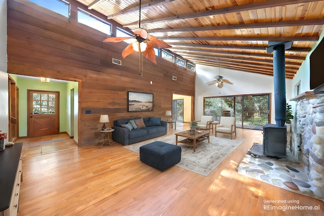 living room featuring high vaulted ceiling, beamed ceiling, a wood stove, ceiling fan, and wood ceiling