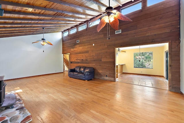 unfurnished living room with ceiling fan with notable chandelier, a wood stove, light wood-type flooring, wood ceiling, and beam ceiling